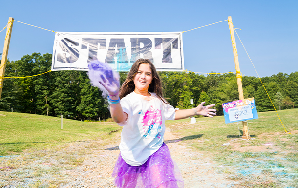 girl in a color run standing in front of a start line throwing purple powder