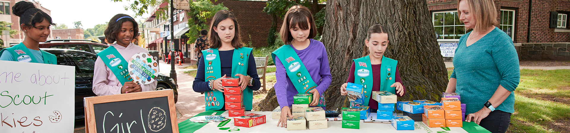  group of ambassador high school girl scouts at outdoor booth selling cookies 