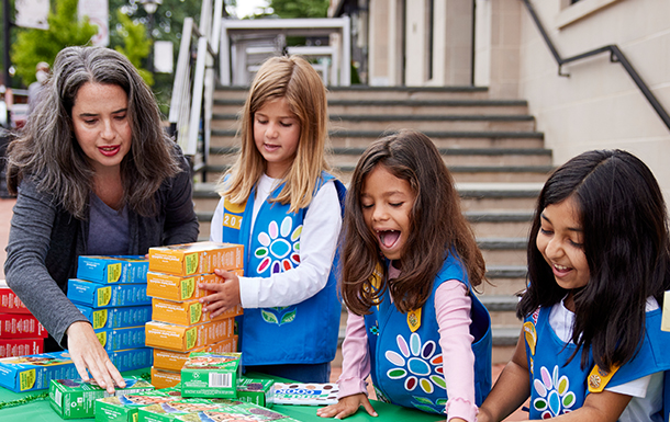 two adult volunteers with a group of girl scout daisies outside selling cookies